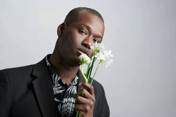 Young man of African ethnicity holding white flowers by his face — Stock Photo, Image