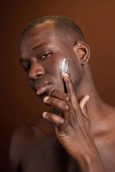 Giovane serio uomo africano applicare crema idratante sul viso — Foto Stock