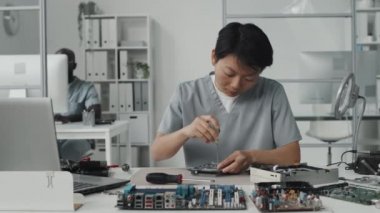 Laboratuvarda çiplerle çalışırken dizüstü bilgisayar ve tornavida kullanan Asyalı kadın mühendis.
