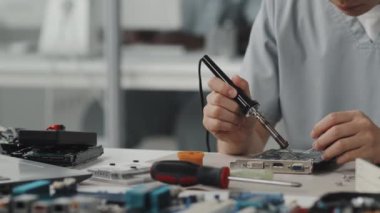 Laboratuvarda çalışırken elektronik bileşenleri lehimleme demiriyle tamir eden kadın mühendisin yakın çekim görüntüleri.