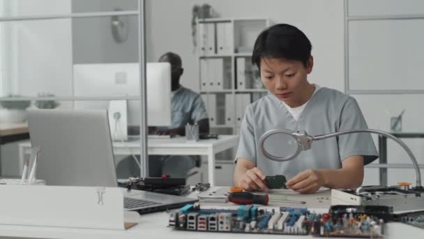 Азиатская Женщина Инженер Сидит Столом Лаборатории Рассматривает Чип Увеличительным Стеклом — стоковое видео