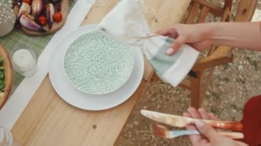 Kırpılmış kadının tabakları peçete ve çatal bıçakla birlikte sofraya koyuşunun en üst görüntüsü. Lezzetli yemekler ve gündüz süsleri.