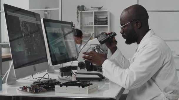 Ingeniero Afroamericano Bata Laboratorio Sentado Escritorio Con Dos Pantallas Computadora — Vídeo de stock