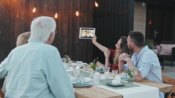 夏の夜に裏庭のテーブルに座っている若いと古い白人女性と男性の中 タブレットコンピュータを使用して家族を呼び出すビデオ — ストック動画