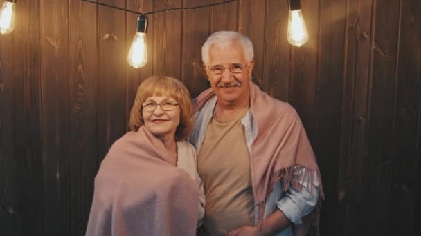 白炽灯下 白种人快乐女人和老人站在木墙边 用毛毯热身 在镜头前微笑的中等肖像画 — 图库视频影像