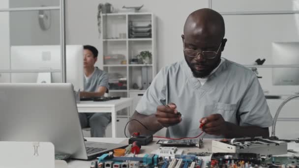 アフリカ系アメリカ人のエンジニアは マルチメータで電子部品をテストし 実験室のデスクでラップトップで作業する — ストック動画