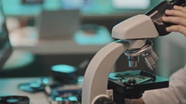 Laboratuvar önlüklü kadın teknik mühendisin mikroskop altında bilgisayar devrelerini incelerken yakın plan çekimleri.