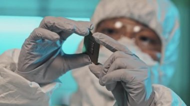 Elektronik mühendisinin eldiven ve tulum giyip bilgisayar çipi tutarken ve incelerken seçmeli odak noktası.