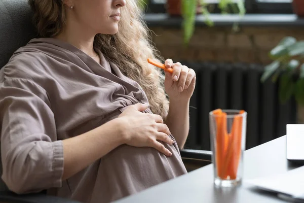 Terhes nő eszik zöldséget a munkahelyen — Stock Fotó