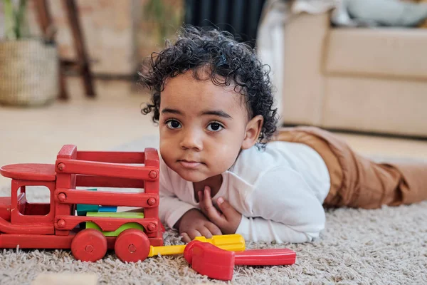 Curly-haired menino deitado perto de carro de brinquedo — Fotografia de Stock