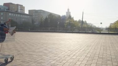 Kot pantolon giyen, içinde dikkatsiz siyahi bir kız olan alışveriş arabasını iten, güneşli bir günde şehirde eğlenen arkadaşları olan mutlu, beyaz bir adam.