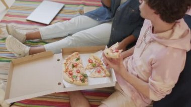 Siyahi kız üniversite öğrencisi ve beyaz erkek arkadaşının gündüz vakti yatak odasında oturup sohbet etmesi, gülümsemesi ve kutudan pizza yemesi.