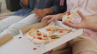 Düşük açılı ağır çekimde, gün ortasında yatak odasında yerde oturan, pizza yiyen, atıştırmalık şeyler yiyen iki arkadaş.