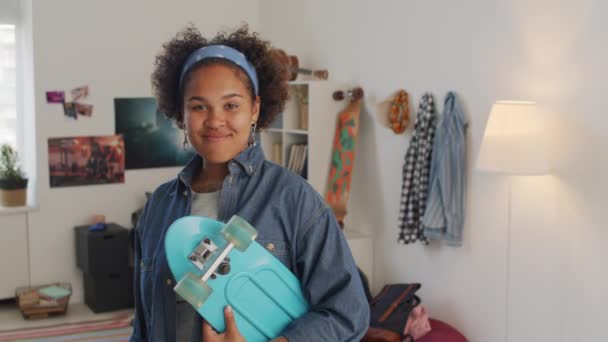 黑色女大学生手持塑料滑板 白天站在卧室里 在镜头前看着和微笑的中间肖像 — 图库视频影像