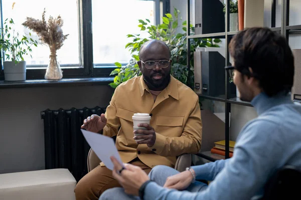 Ung afroamerikansk man konsulterar sin kollega med papper — Stockfoto