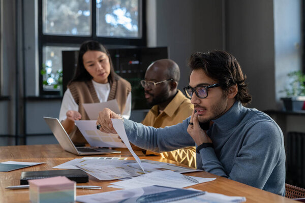 Молодой занятой экономист с мобильным телефоном просматривает данные в документе