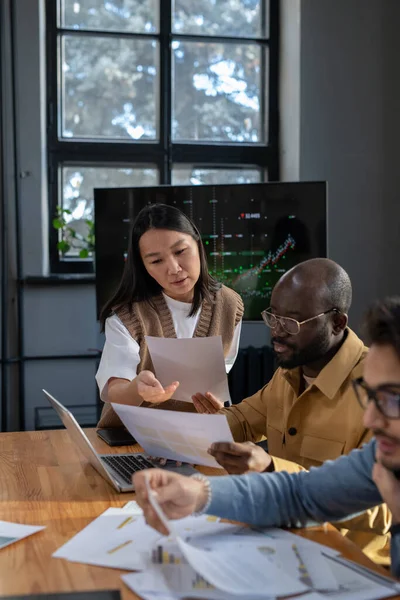 Young confident Asian businesswoman with paper consulting male colleague — Stock Photo, Image