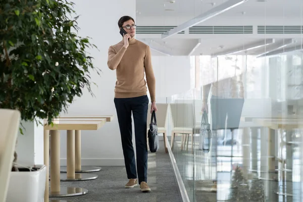 Junger Geschäftsmann mit Handtasche und Smartphone im Büro — Stockfoto