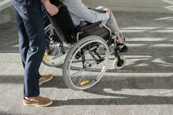 Młody elegancki biznesmen stojący za wózkiem inwalidzkim z koleżanką — Zdjęcie stockowe