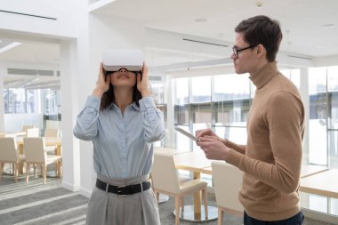 Tabletli genç işadamı VR gözlüklü bayan meslektaşının yanında duruyor.