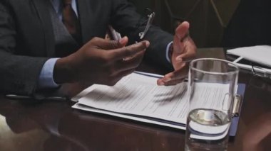 Resmi takım elbiseli, elinde gözlüklü ve toplantı masasında anlaşma şartlarını açıklayan tanınmamış Afro-Amerikan sözleşme avukatının yakın çekimleri.