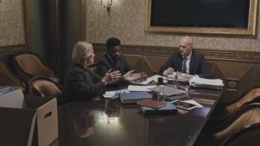 Bir grup çok ırklı profesyonel avukatın toplantı masasında oturup kağıtları tartışmalarını yakınlaştırın.