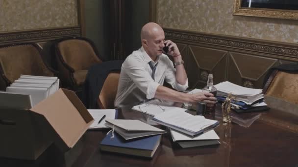 서류가 식탁에 앉아서 사무실에서 일하는 휴대폰으로 통화하고 유리에 위스키를 중년의 — 비디오