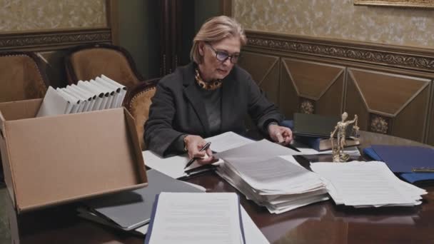 オフィスのテーブルに座って書類を調べる先輩女性弁護士のショットを下に傾ける — ストック動画