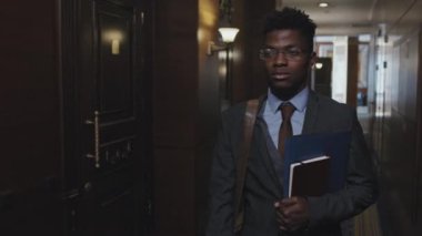 Ofis koridorunda dosya klasörü ve not defteriyle yürürken Afrikalı Amerikalı iş adamının iş arkadaşını selamlarken belden yukarısını çek.