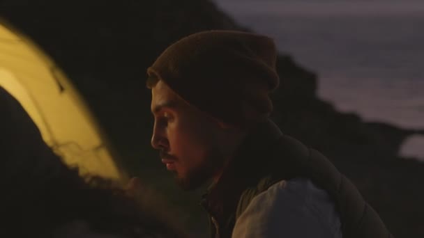 男人和女人在湖边的营地里度过夜晚 坐在篝火边谈论某事的横向镜头 — 图库视频影像