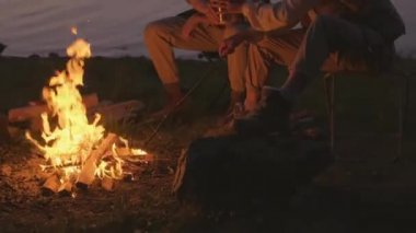 Kadın ve erkeğin kamp alanında kamp ateşinin yanında oturup çay içerken çekilmiş yatay görüntüsü.