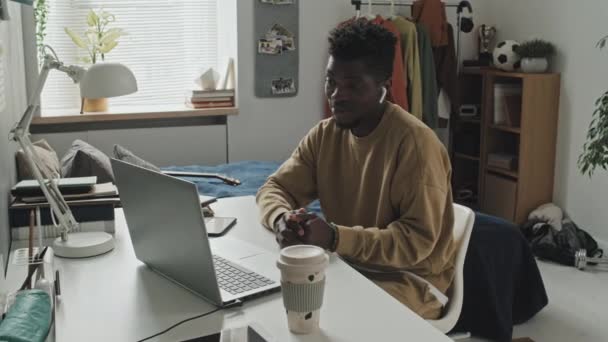 Bogenaufnahme Eines Jungen Afroamerikaners Mit Drahtlosen Kopfhörern Der Schreibtisch Sitzt — Stockvideo