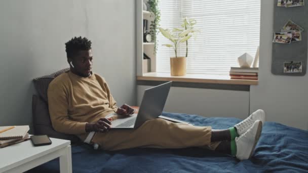 Junger Afroamerikaner Mit Drahtlosen Kopfhörern Sitzt Hause Auf Dem Bett — Stockvideo