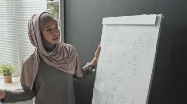 Tesettürlü Müslüman bir kadın tecrit sırasında çevrimiçi öğretmenlik yaparken ters çizelgede matematik formüllerini anlatıyor