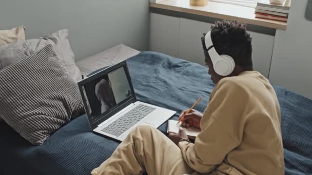 Hombre Afroamericano Auriculares Inalámbricos Acostado Cama Casa Escuchando Tutora Escribiendo — Vídeos de Stock