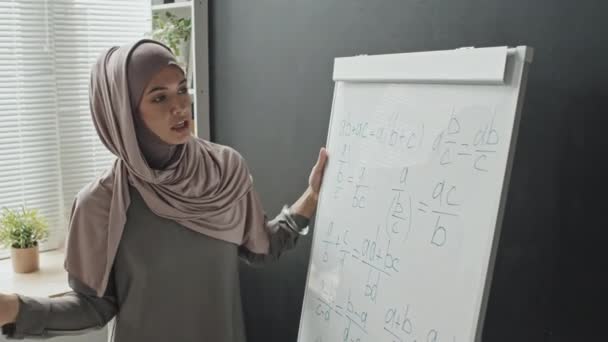 在封锁期间 穆斯林妇女在网上授课时 戴着头巾 在流程图上解释数学公式 — 图库视频影像