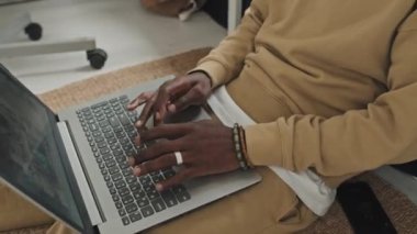 Afrika kökenli Amerikalı bir adamın kablosuz kulaklıklarıyla yatak odasında otururken ve bilgisayarında yazarken evden ya da e-öğrenirken.