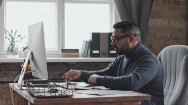 Ortadoğulu iş adamı bilgisayarda görüntülü konuşma yapıyor, sonra gözlüğünü çıkarıyor ve işten yorulurken gözlerini ovalıyor.