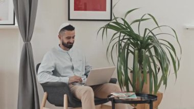 Kufi 'deki Müslüman adam evdeki koltukta oturuyor ve bilgisayardaki video konuşmasında konuşuyor.