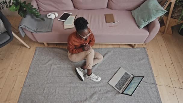 自上而下拍摄的非洲裔美国女孩坐在客厅的地板上 一边在家里远程学习 一边用笔记本电脑通过在线视频通话 — 图库视频影像