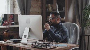 Orta Doğulu bir adam ofis masasında oturmuş bilgisayardan iş projesini tartışıyor.