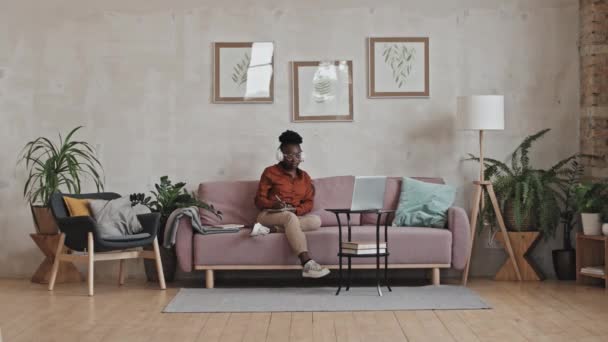 Kablosuz Kulaklıklı Genç Afrikalı Bir Kadının Oturma Odasındaki Kanepede Oturup — Stok video