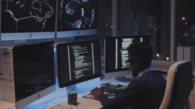 Genç siyahi erkek programcının yan görüntüsü. Geceleri büyük şehirde masa başında bilgisayar kodu üzerinde çalışıyor.