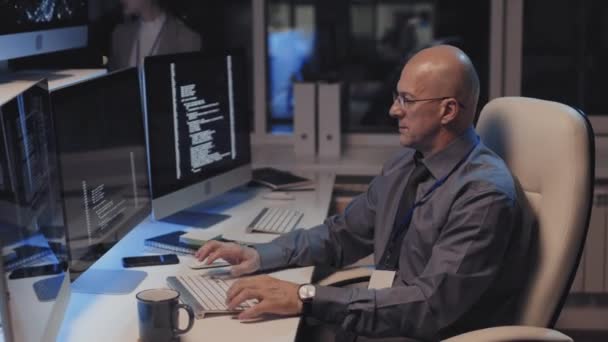 成熟的白种人男性网络安全专家头戴眼镜 身穿正式服装 晚上坐在办公桌前 在个人电脑上进行编码的侧视图 — 图库视频影像