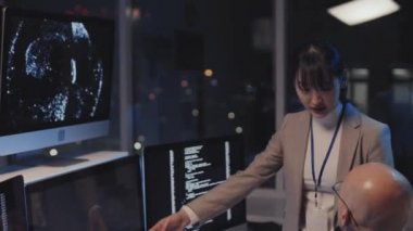 Genç Asyalı kadın yöneticinin resmi giysiler giymesini beyaz erkek programcıyla konuşmasını geceleri şirket ofisinde bilgisayar kullanarak masa başında oturmasını.