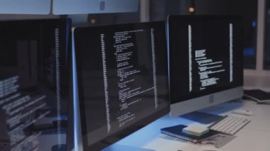 Bilgisayarda çalışan bilgisayar kodlu bir program, geceleri boş ofisteki masada duran birden fazla monitör
