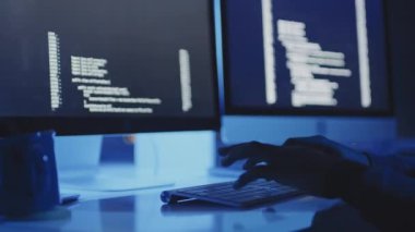 Karanlık modern ofiste masa başında oturan, klavyeye yazı yazan, bilgisayarda kodlayan kırpık erkek programcının düşük açısı.