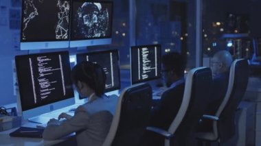 Karanlık modern ofisteki koltuklarda oturan, geceleri bilgisayarlar üzerinde çalışan üç farklı programcının yan görüntüsü