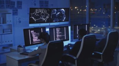Karanlık modern ofisteki koltuklarda oturan, geceleri bilgisayarlarda kod yazan üç çoklu etnik programcının arkası
