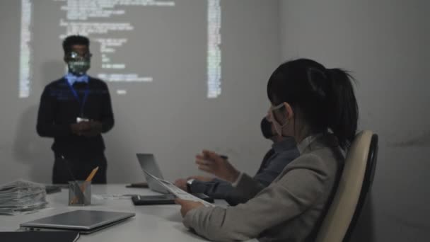 カスタムメイドのフェイスマスクを身に着けている若い黒の男性ソフトウェアエンジニアの中長期 それにコンピュータコードの投影と白い壁に立って プレゼンテーションを作ります アジアの女性は質問を投げかけます — ストック動画